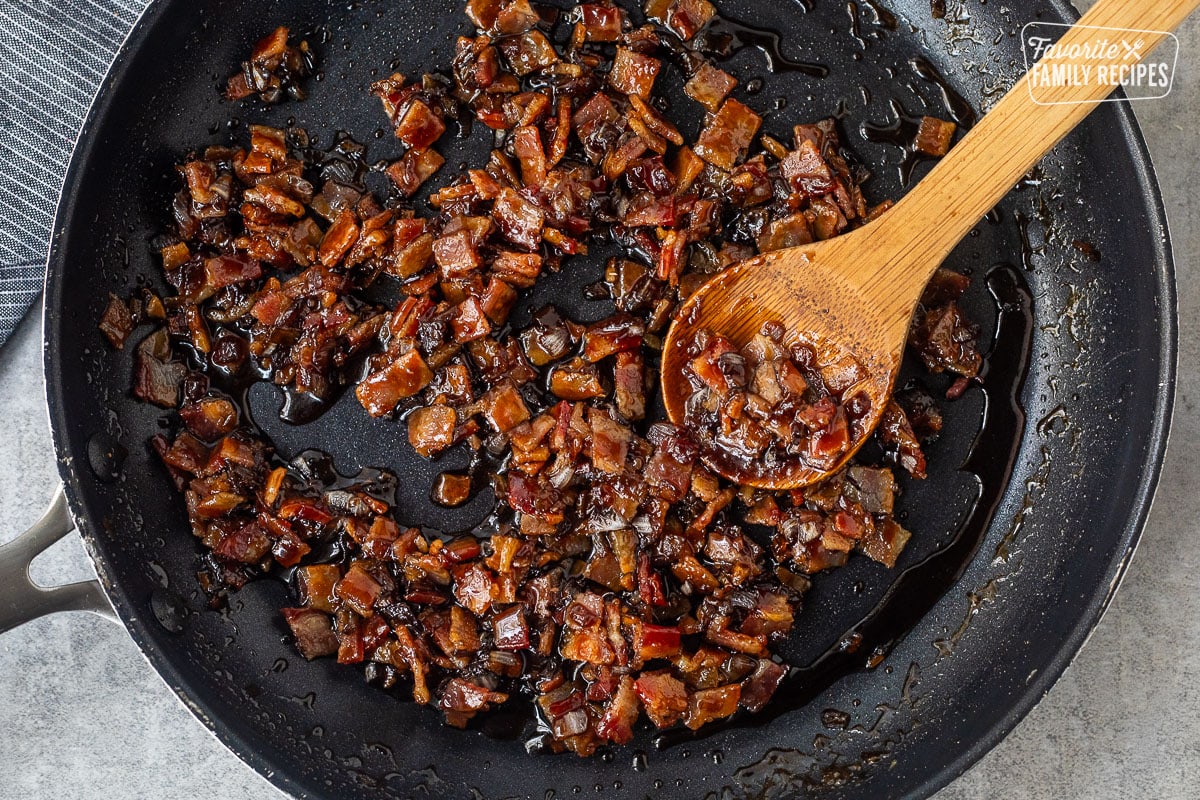 Cooked bacon jam with a wooden spoon in a black skillet