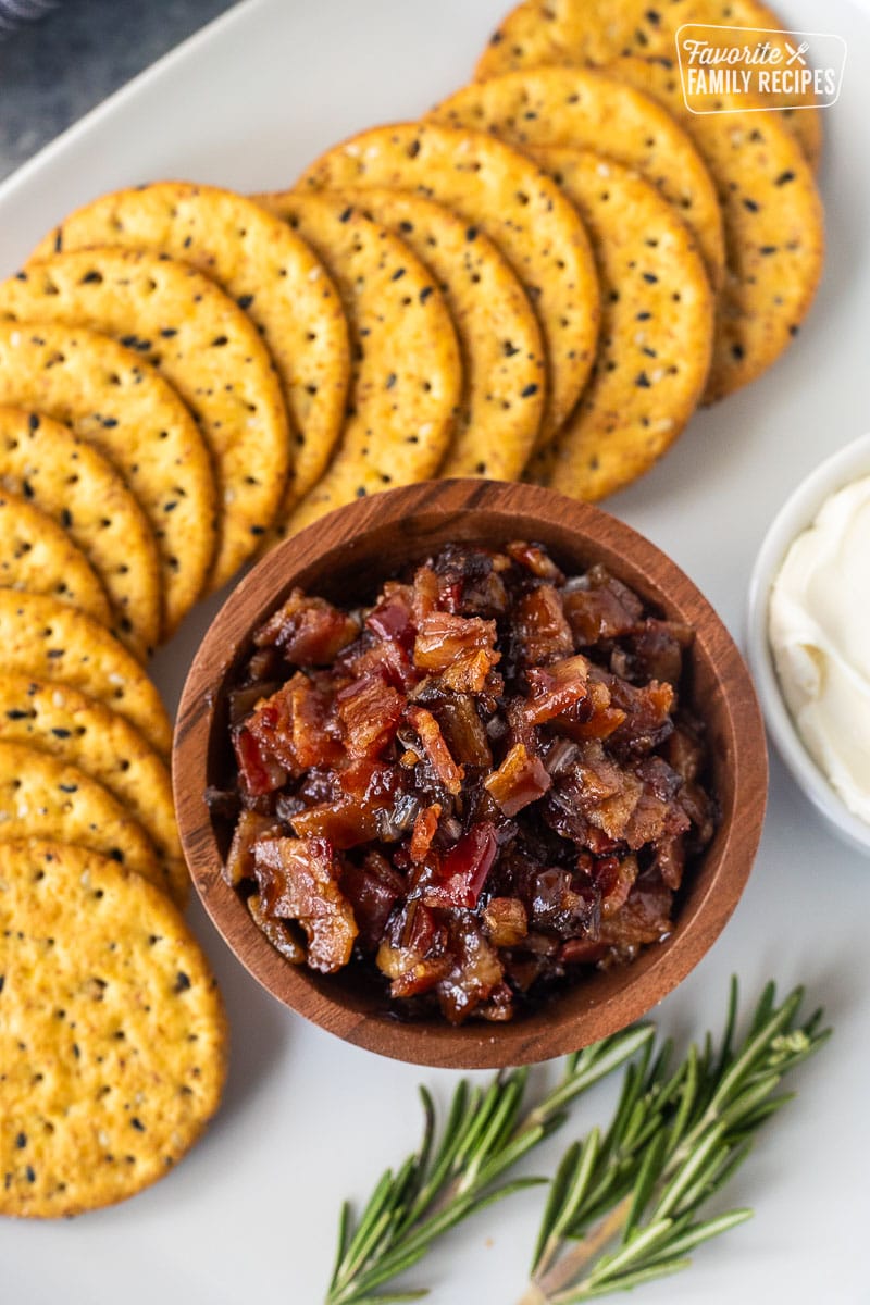 Wooden bowl of bacon jam next to crackers and cream cheese.