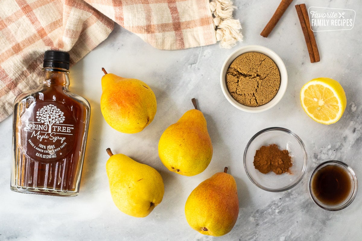 Ingredients to make baked pears including maple syrup, dark, brown sugar, lemon, cinnamon, apple pie spice, vanilla, and pears.