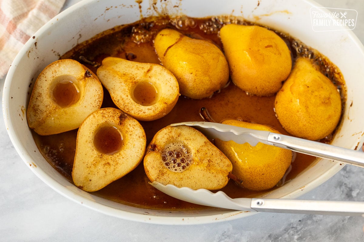 Using tongs to flip baked pears in a baking dish.