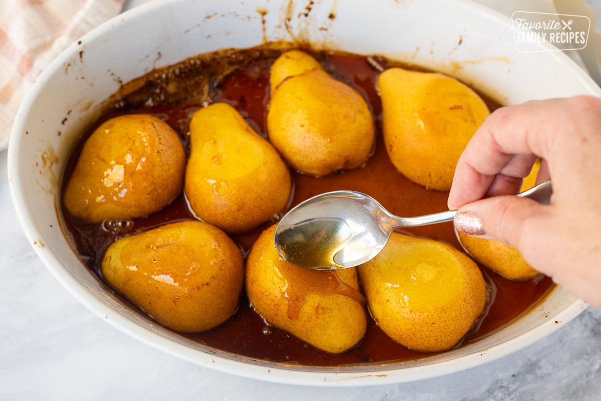 Pouring caramel syrup over baked pears in a baking dish.