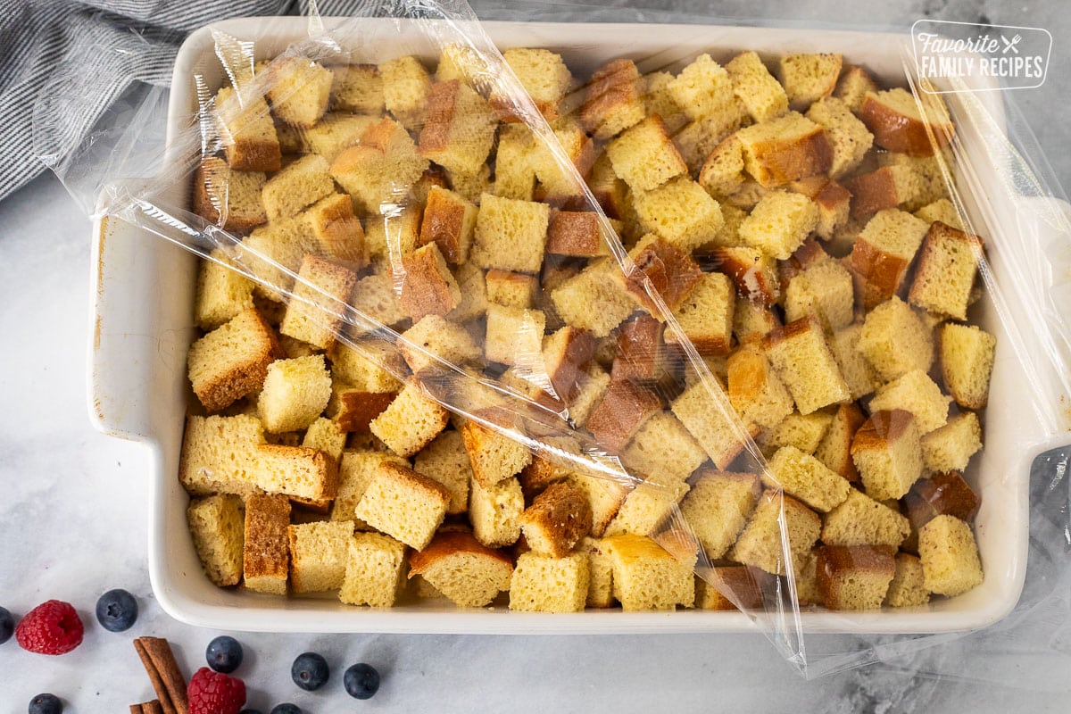 Plastic wrap on top of a baking dish of unbaked brioche French casserole.