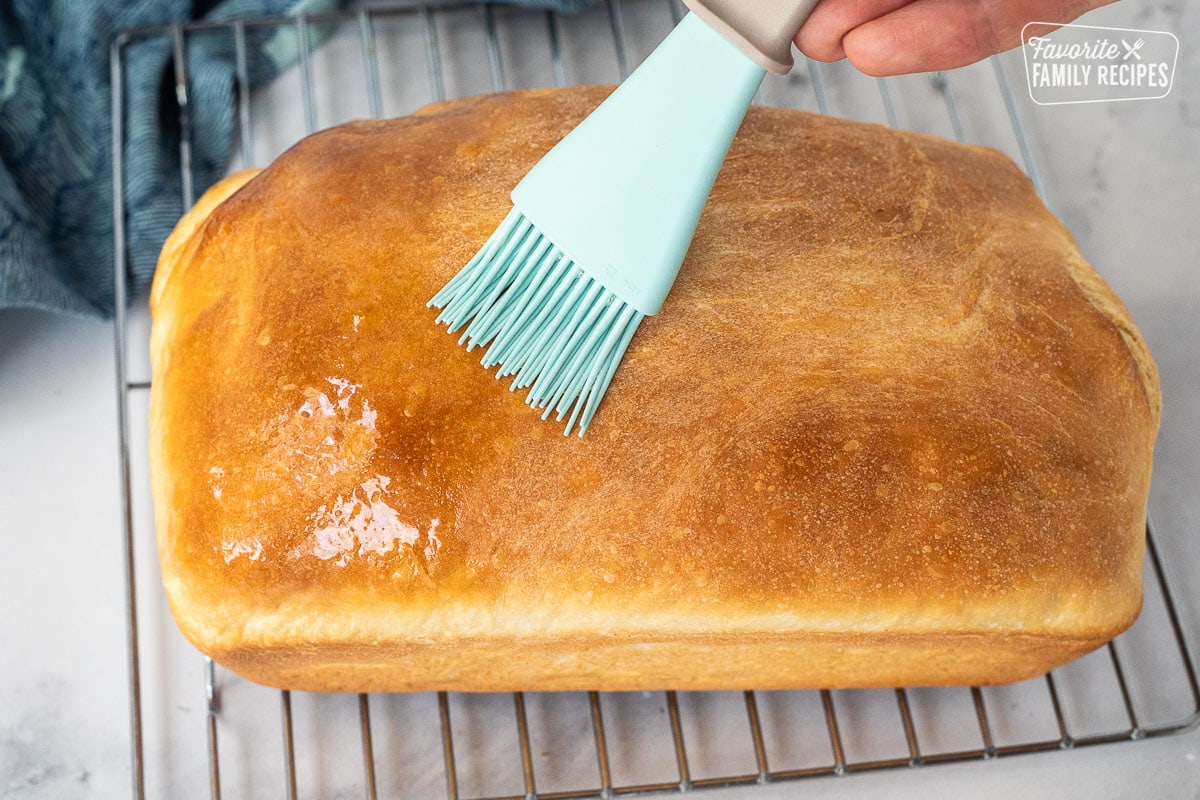 Brushing butter onto baked bread loaf.