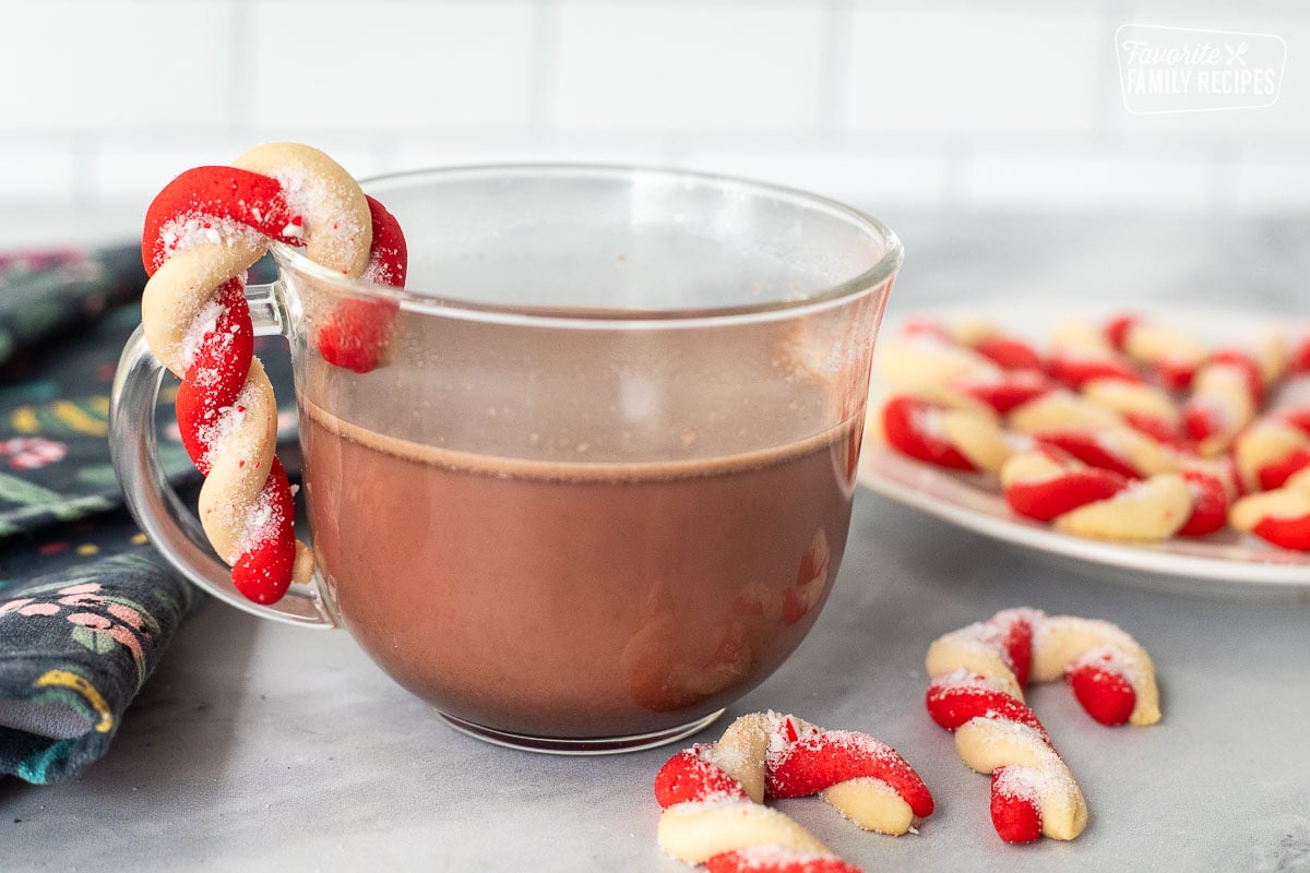 A cup of cocoa with a candy cane cookie hanging off the edge