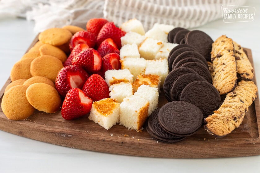 Cutting board with strawberries, angel food cake, Oreos, cookies, and vanilla wafers.