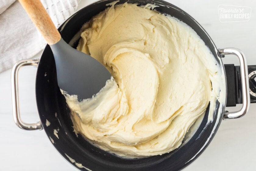 Melted white chocolate chips in fondue pot with spatula.