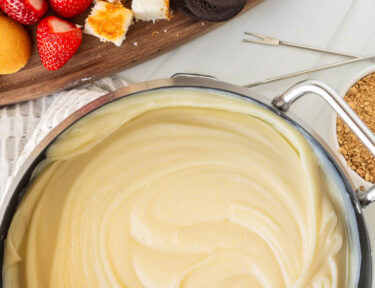 Cheesecake Fondue next to cutting board of cookies, cake and strawberries.