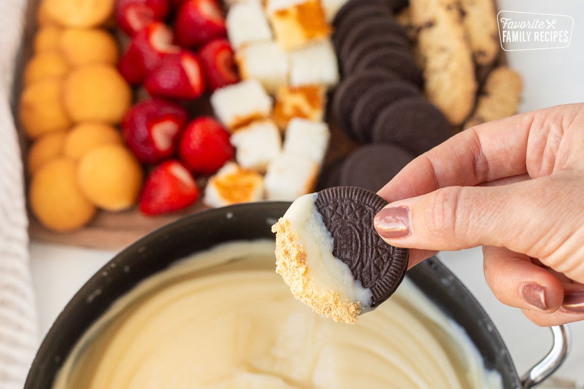 Hand holding an Oreo cookie dipped in Cheesecake Fondue.