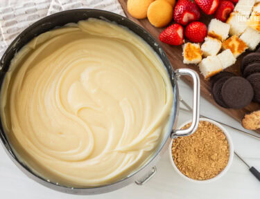 Cheesecake Fondue next to cutting board of cookies, cake and strawberries.