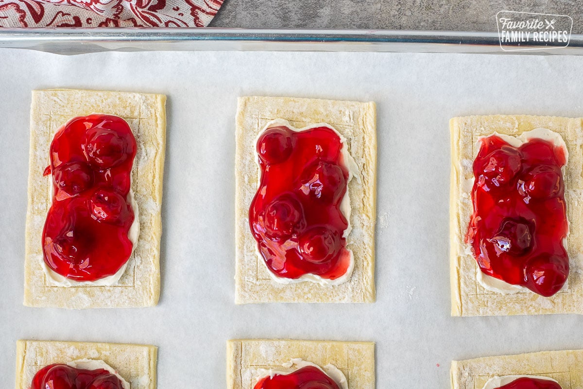 Unbaked puff pastry rectangle with cream cheese, spread in the center and cherry pie filling in the center.