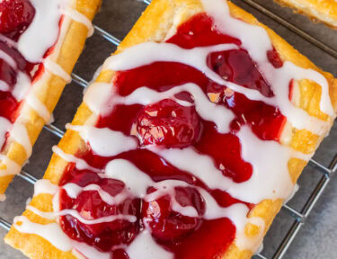 Cherry danish drizzled with white icing on a cooling wired rack.