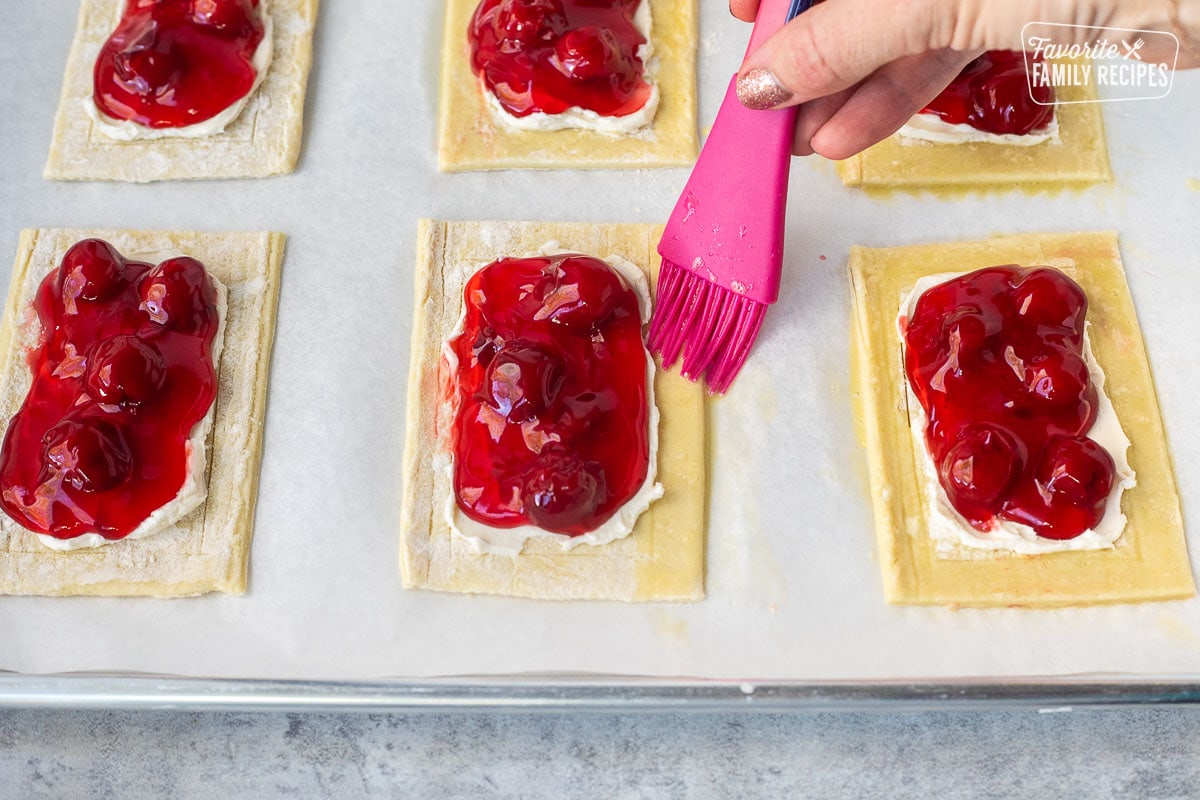 Brushing egg wash onto outside edge of unbaked cherry danish.