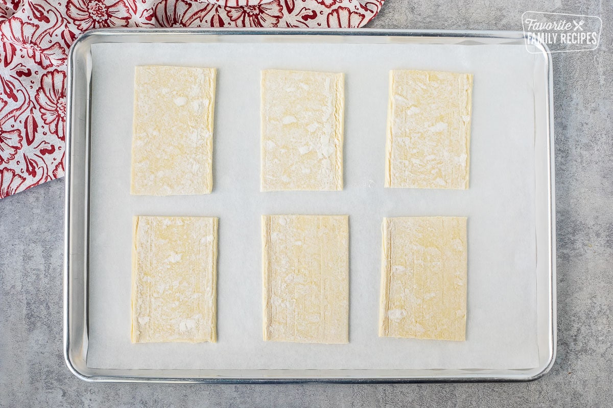 Baking sheet lined with parchment paper and six angled shaped puff pastry.