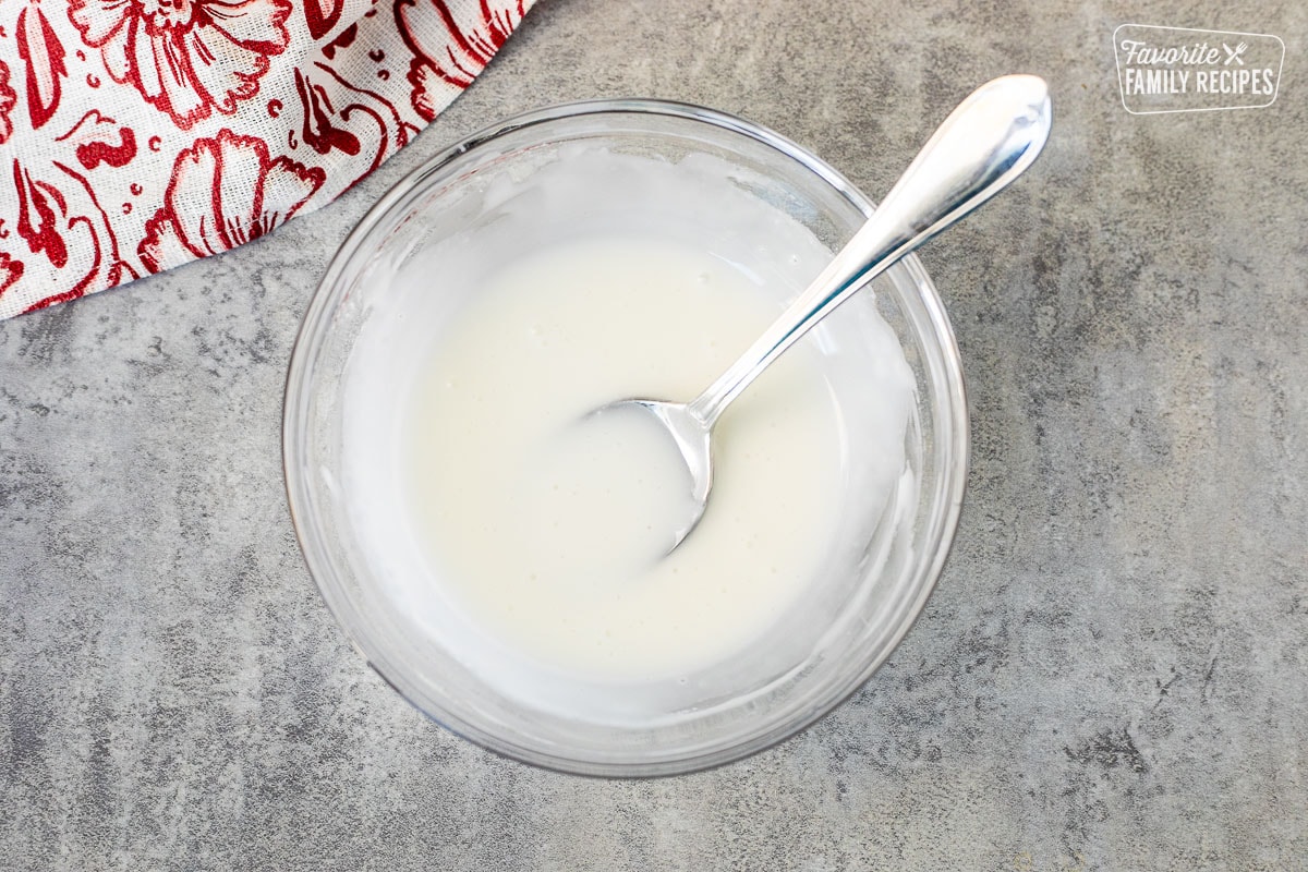 Glass mixing bowl with white icing and a spoon.