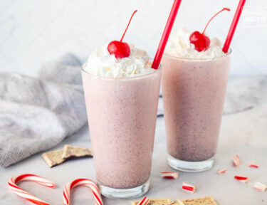 Two glasses of Chick Fil A Peppermint Milkshake topped with whipped cream and a cherry.