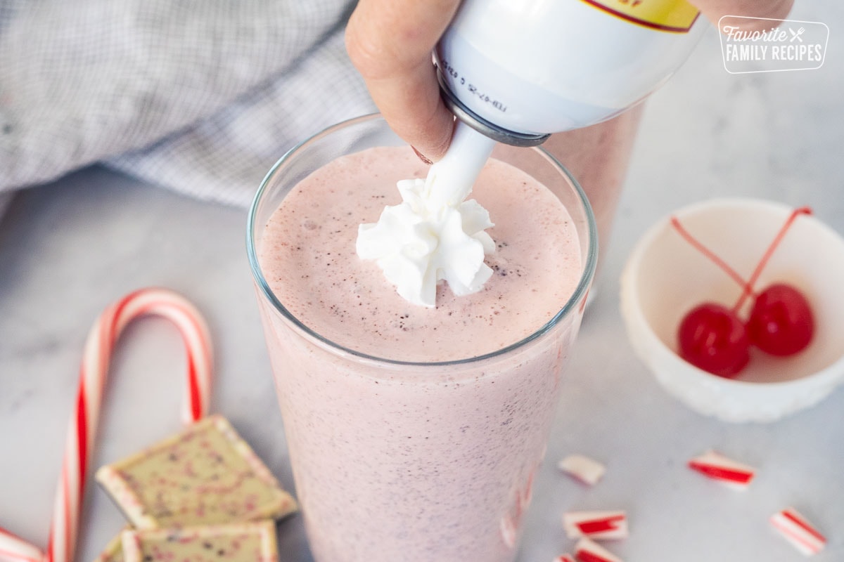 Spraying whipped cream on top of a Chick Fil A Peppermint Milkshake in a glass.