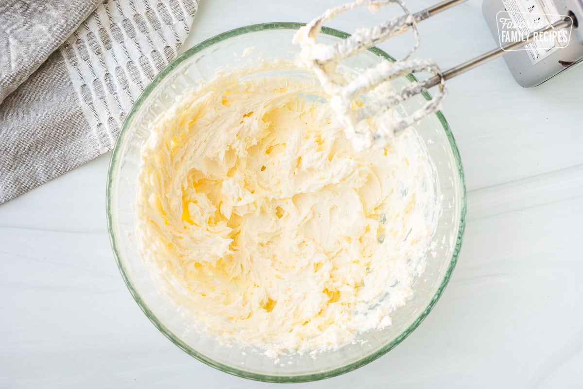 Mixing bowl with butter and cream cheese combined with an electric mixer.