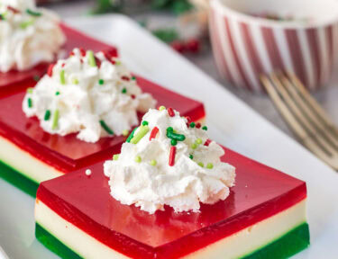 Christmas Jell-O salad slice on a plate with whipped cream and sprinkles.