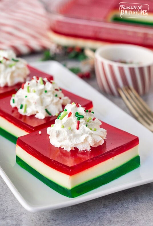 Christmas Jell-O salad slice on a plate with whipped cream and sprinkles.