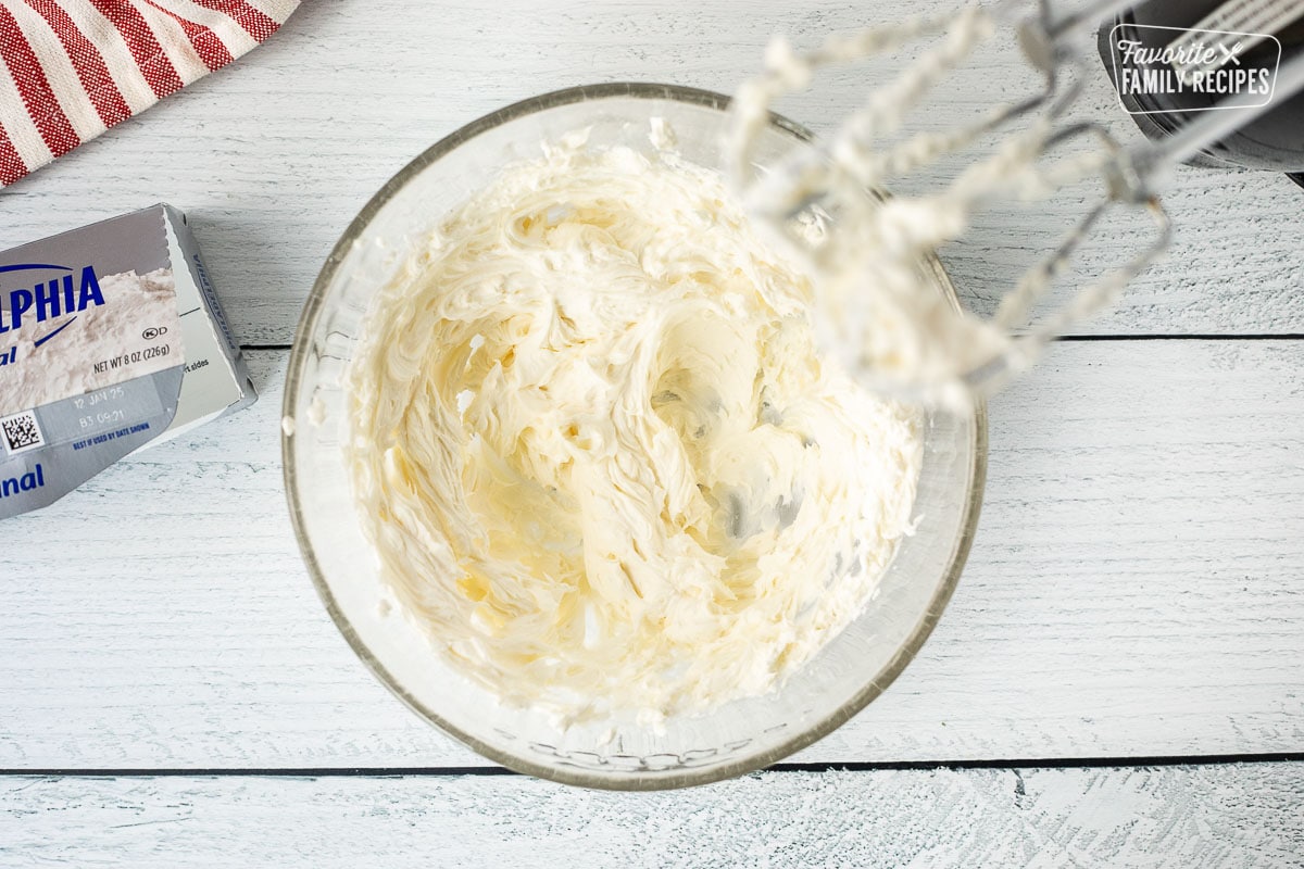 Glass mixing bowl with whipped cream cheese and electric beaters.