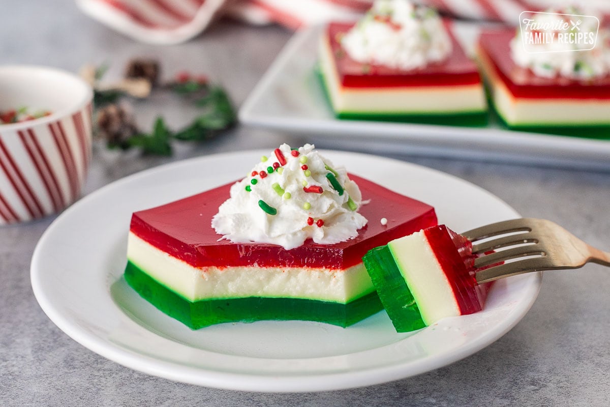 Fork cut into a slice of Christmas Jell-O salad topped with whipped cream and sprinkles.