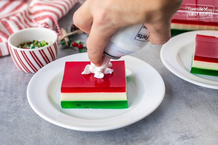 Pressing whipped cream on a slice of Christmas Jell-O salad.