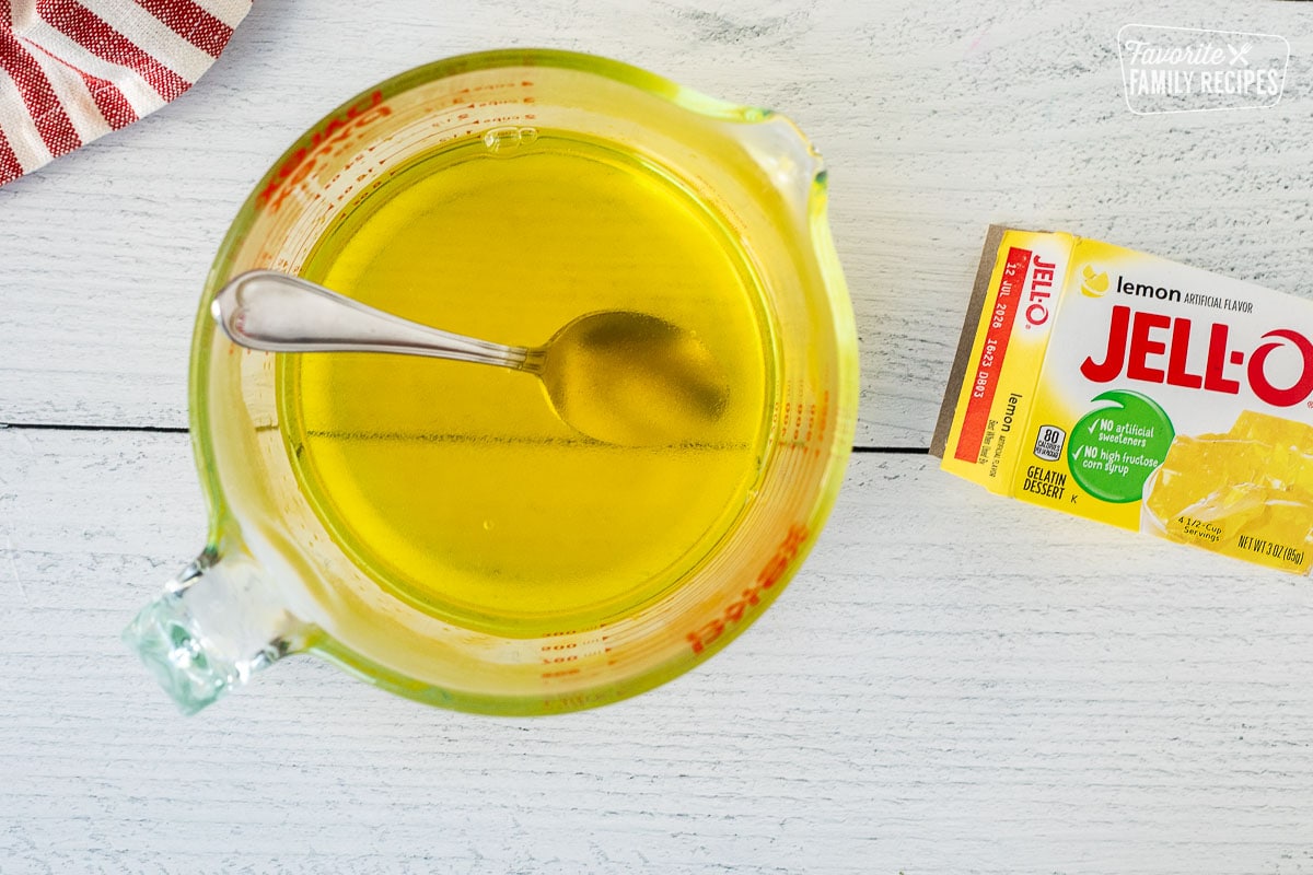 Glass mixing bowl with lemon Jell-O dissolved and a spoon.