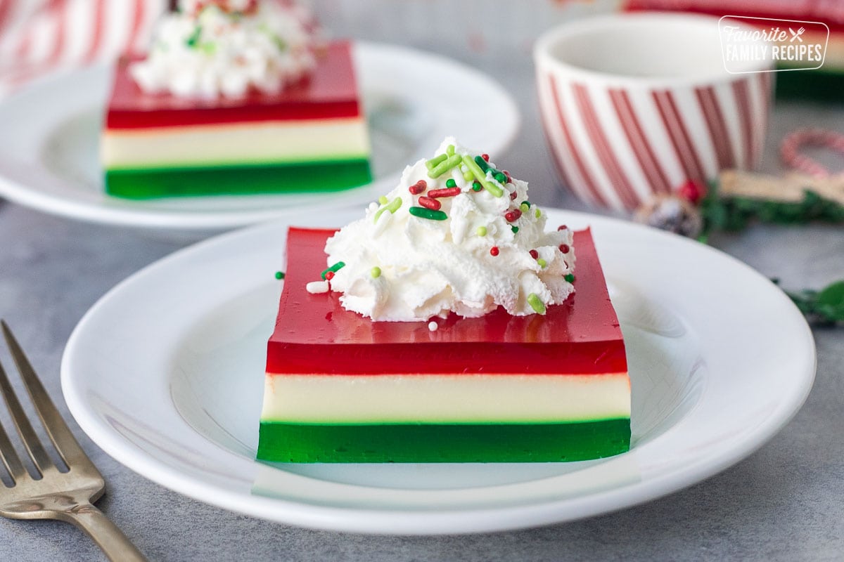 Christmas Jell-O salad slice on a plate with whipped cream and sprinkles.