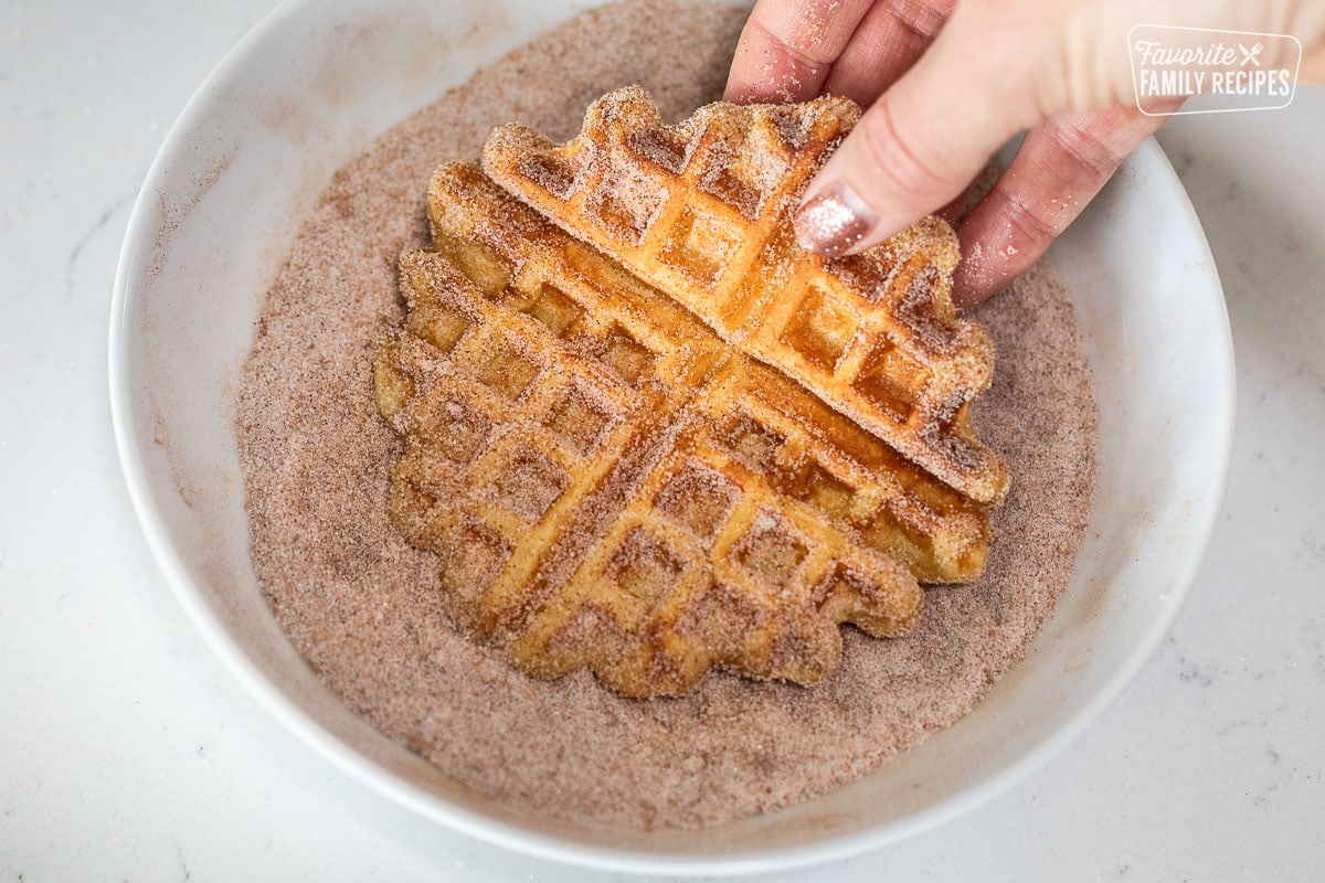 Dipping a hot waffle in a bowl of cinnamon sugar.