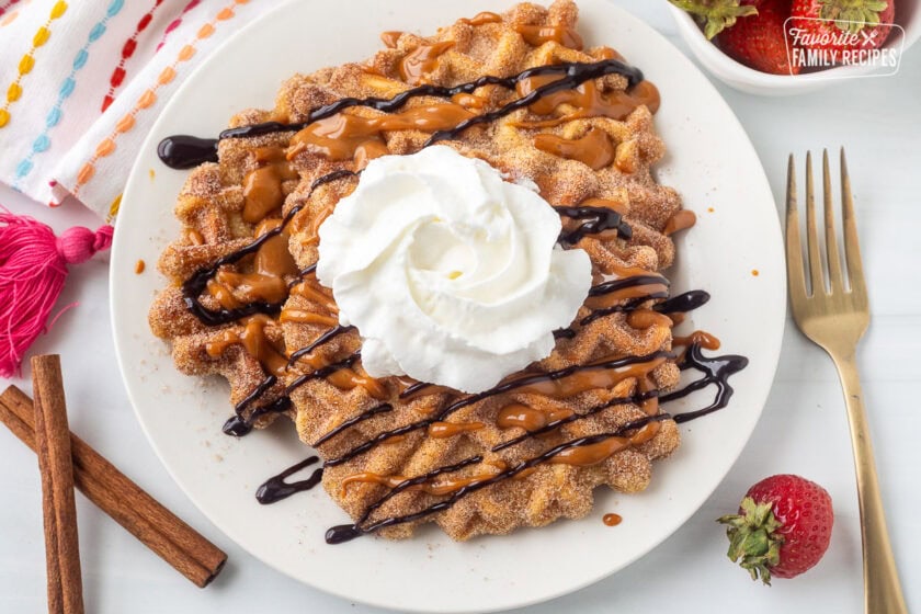 Plate of churro waffles with chocolate and caramel sauce on top and whipped cream.