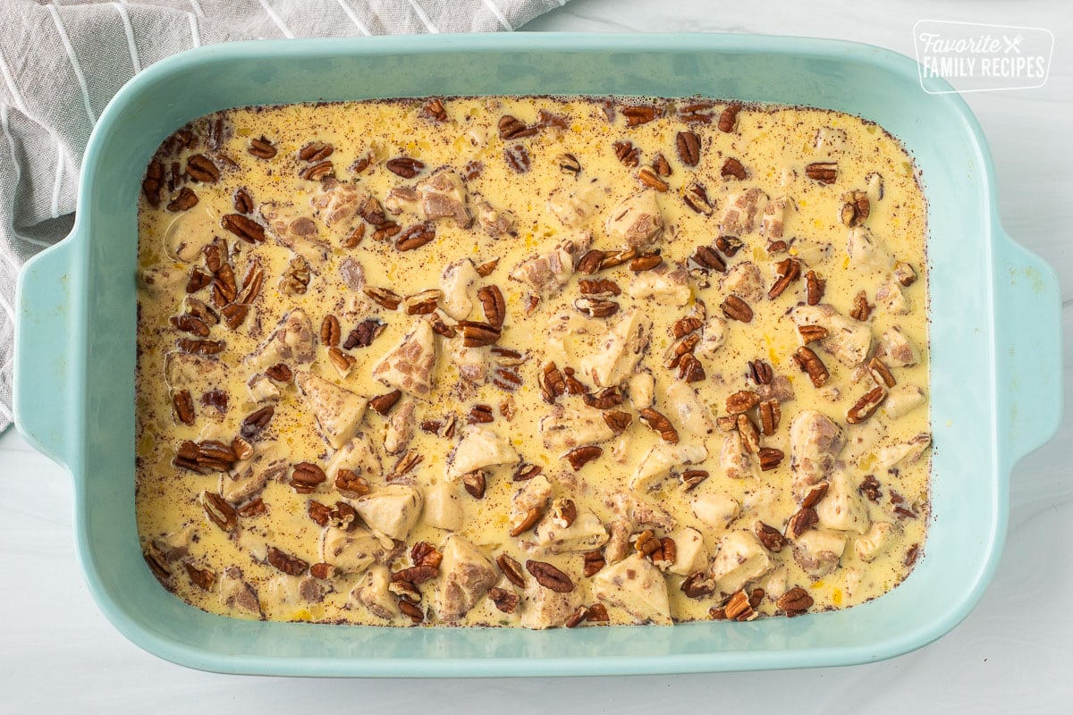 Baking dish with cut up cinnamon rolls, eggs mixture and pecans on top.