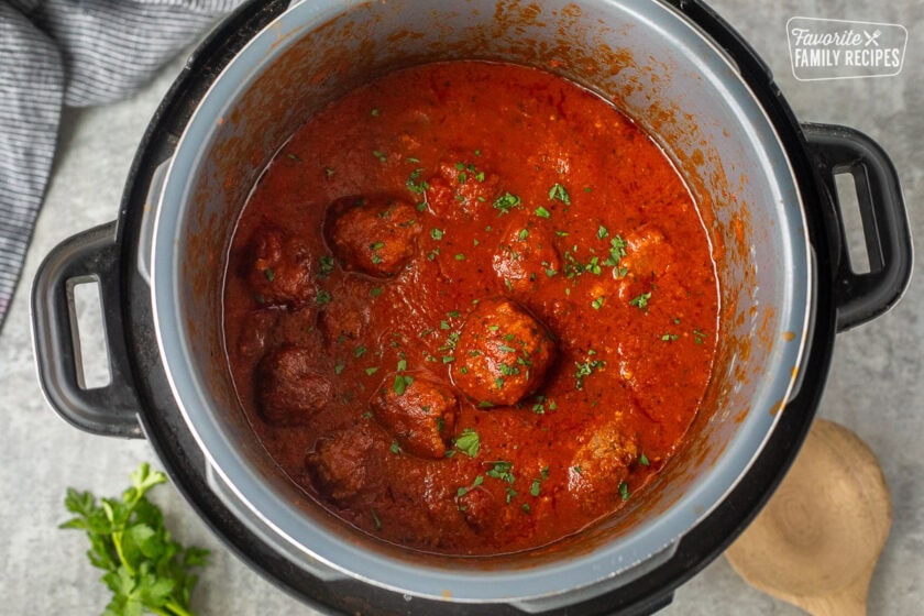 Instant pot with cooked meatballs and marinara sauce garnished with parsley.