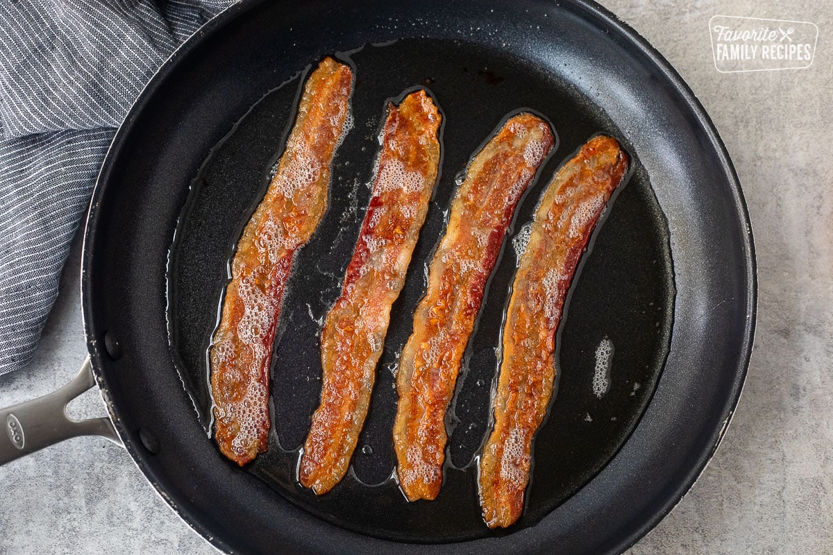 Cooking strips of bacon in a black skillet.