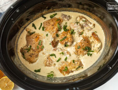 Crockpot with cooked garlic Parmesan chicken and garnished with basil.