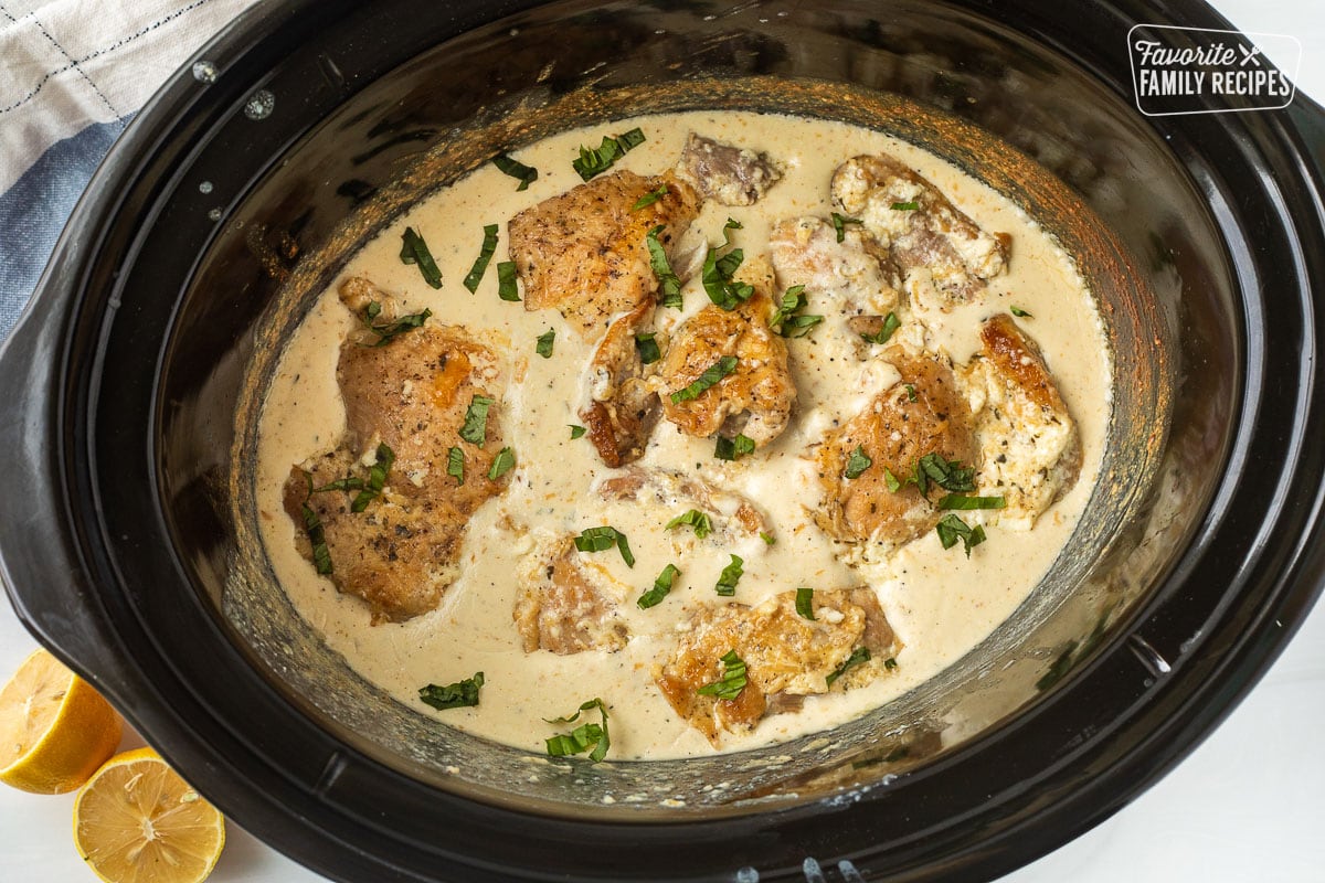 Crockpot with cooked garlic Parmesan chicken and garnished with basil.