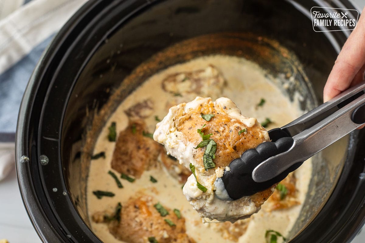 Tongs holding up a piece of crock pot garlic Parmesan chicken.