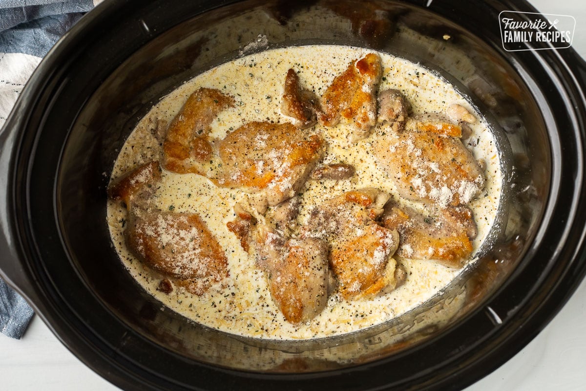 Seared chicken thighs and a crock pot with creamy soup base and a packet of ranch dressing sprinkled on top.