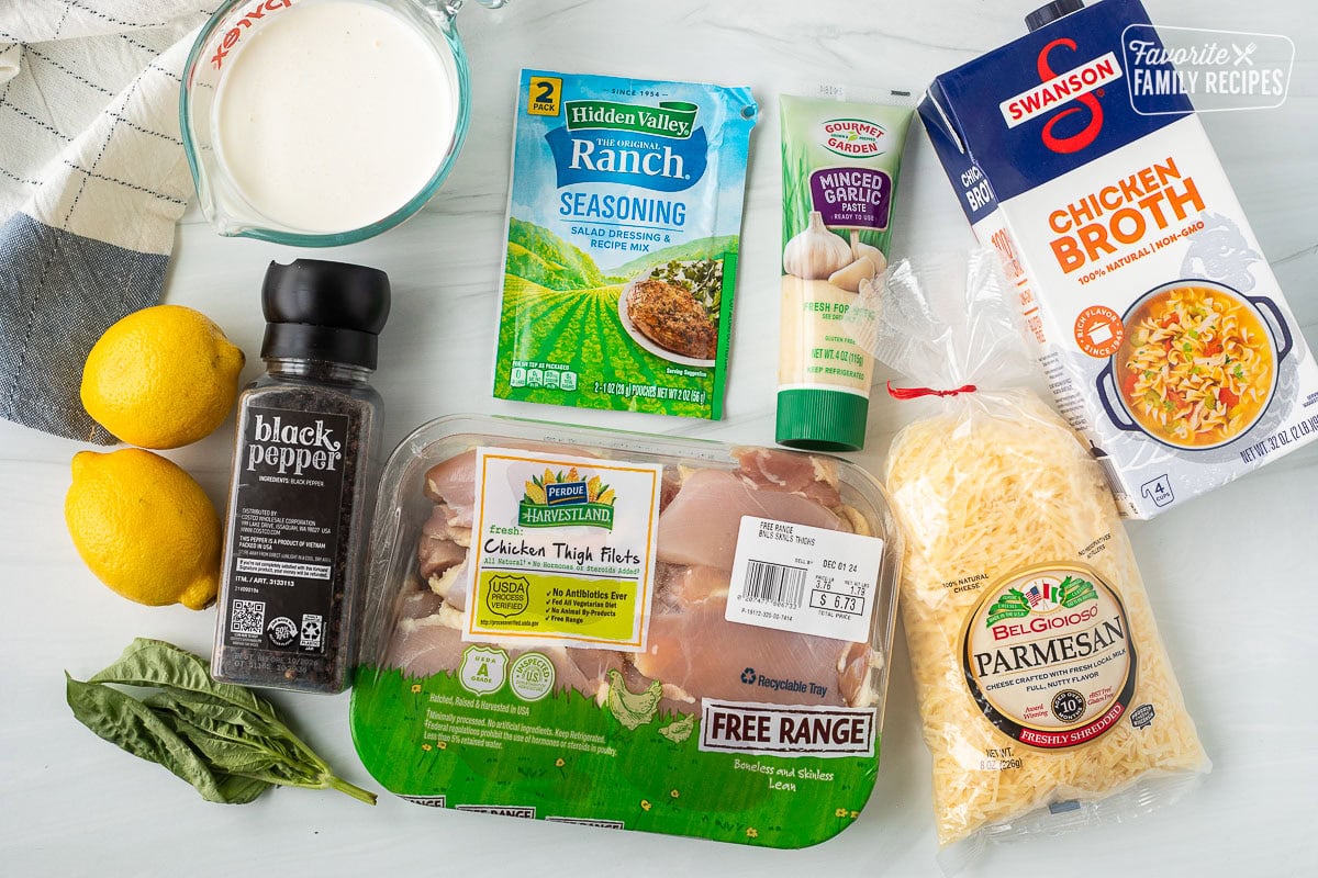 Ingredients to make crockpot garlic Parmesan chicken including chicken thighs, shredded Parmesan cheese, chicken broth, garlic, ranch seasoning packet, cream, lemon, black pepper and basil.