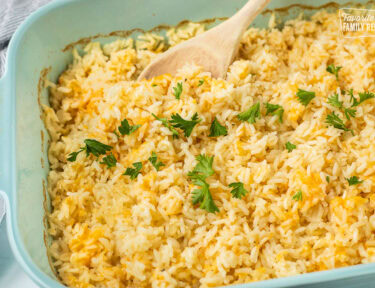 Cheesy rice in a casserole dish with parsley and a wooden spoon.