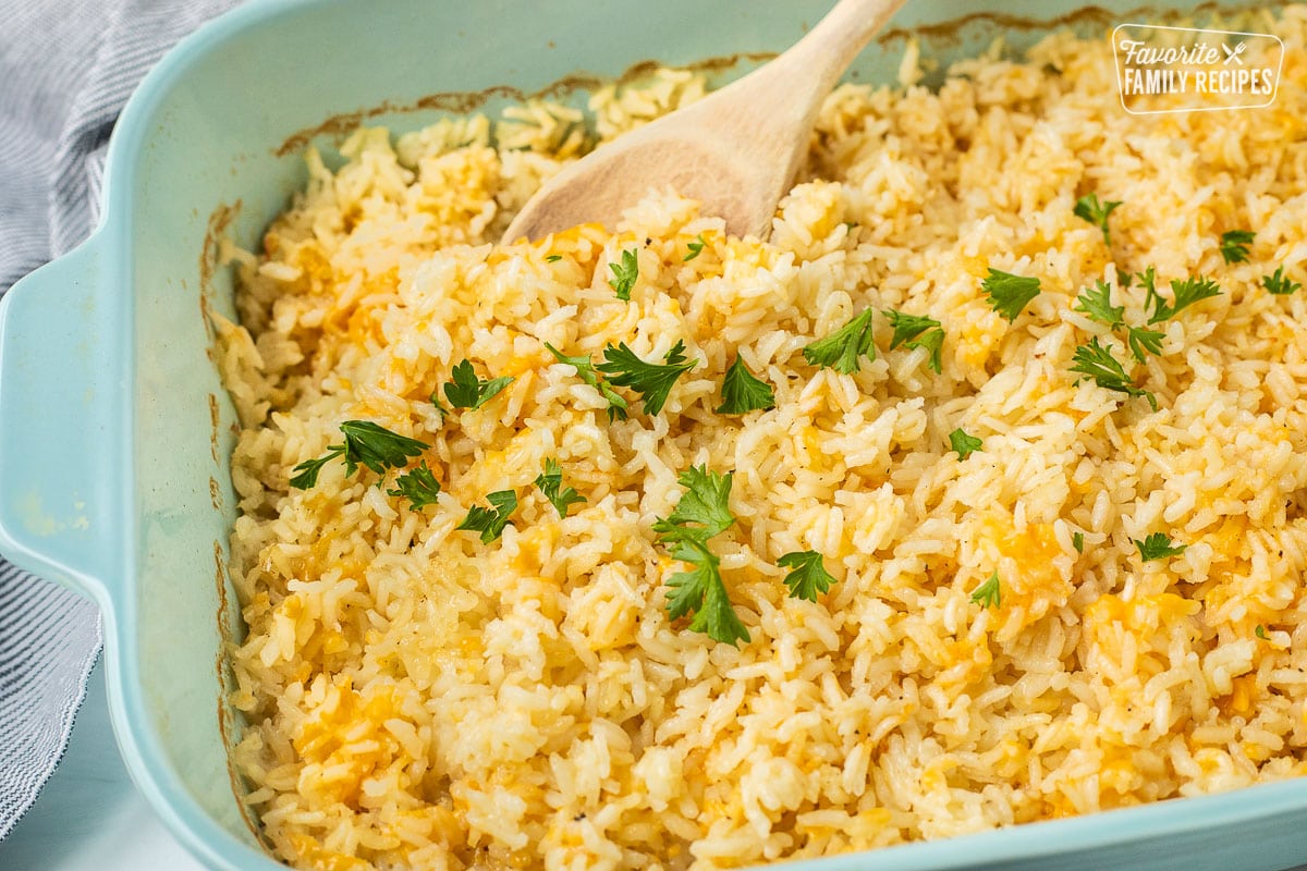 Cheesy rice in a casserole dish with parsley and a wooden spoon.