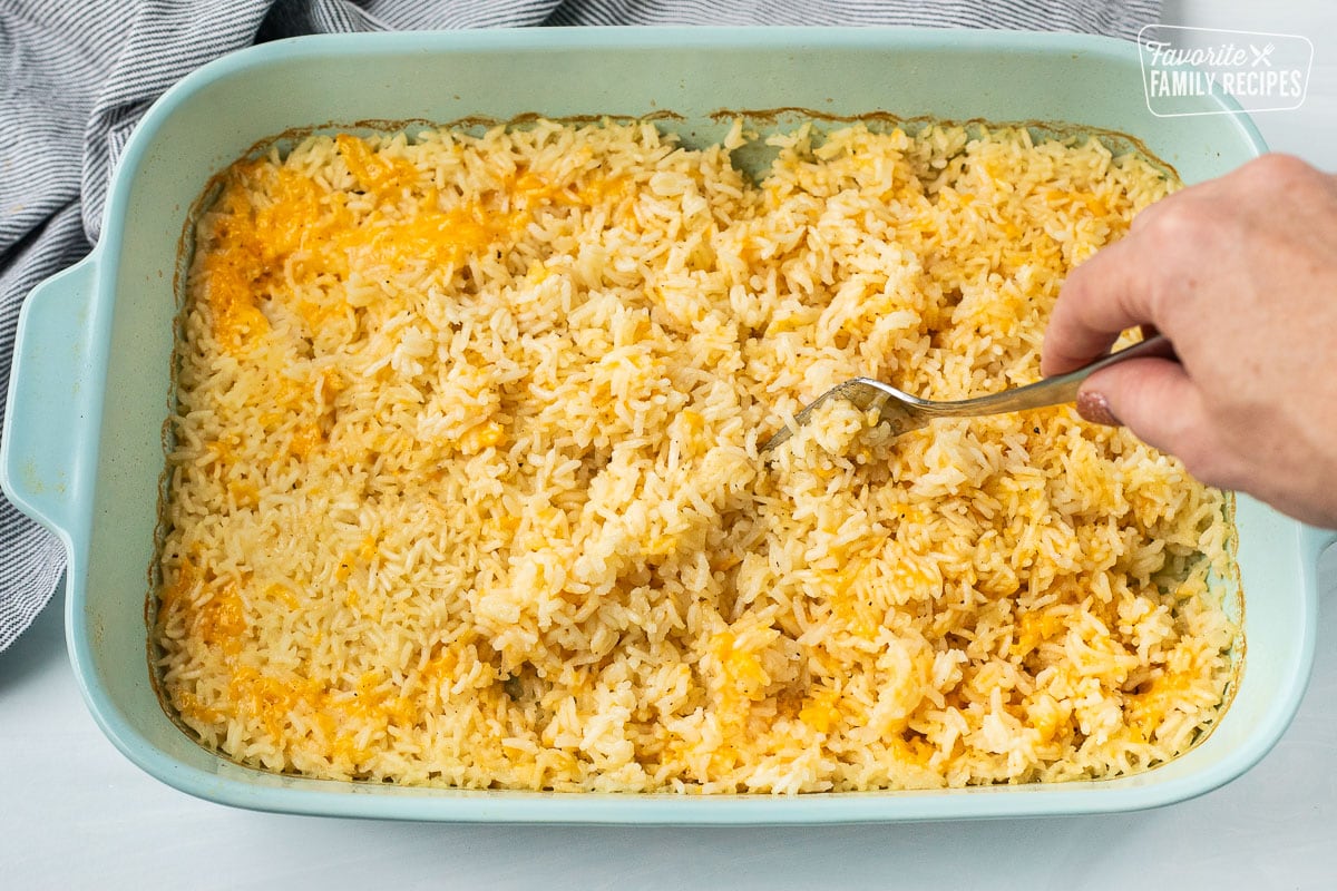 Fluffed cheesy rice with a fork in a casserole dish.