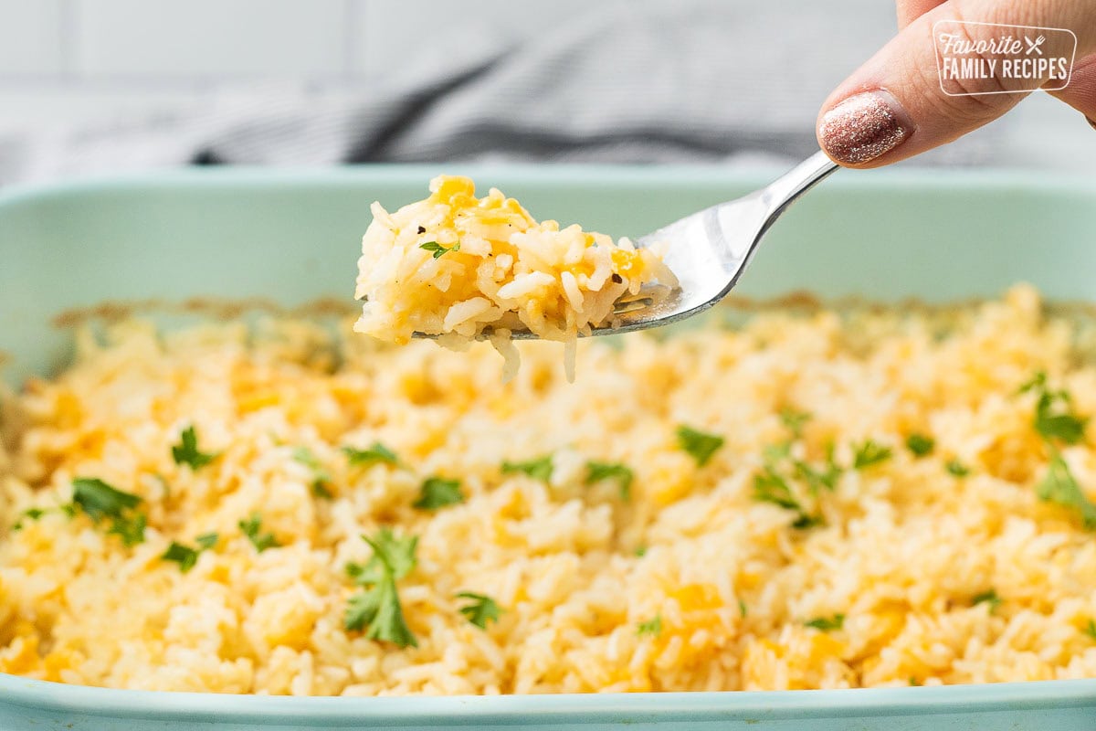 Fork with cheesy rice over casserole dish garnished with parsley.