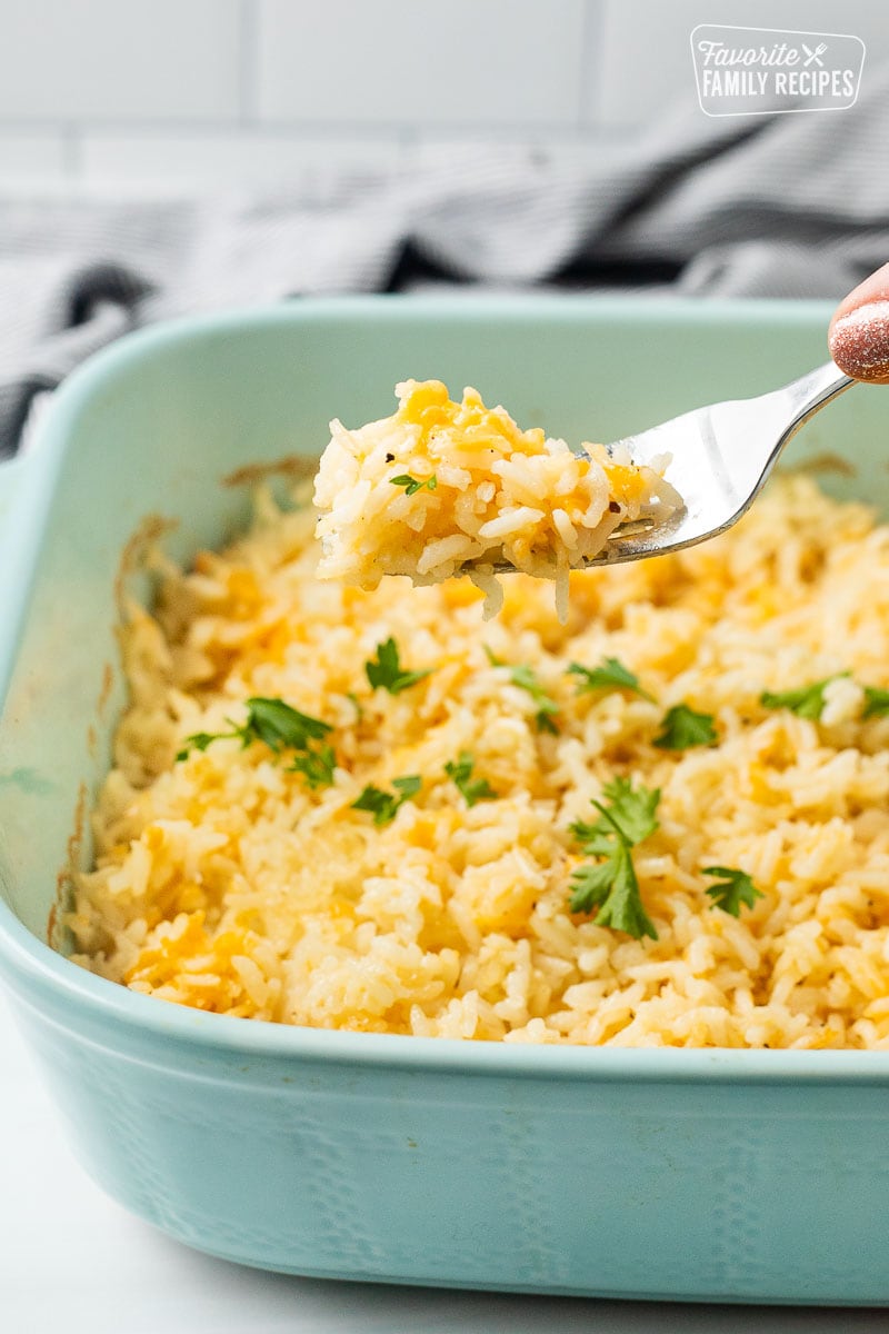 Fork with cheesy rice over casserole dish garnished with parsley.