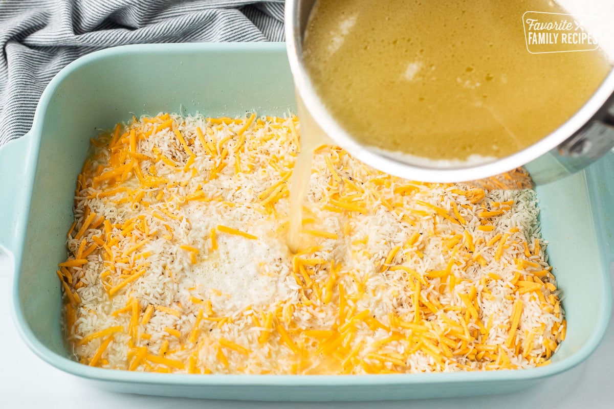 Pouring chicken broth butter over casserole dish of uncooked rice and butter.