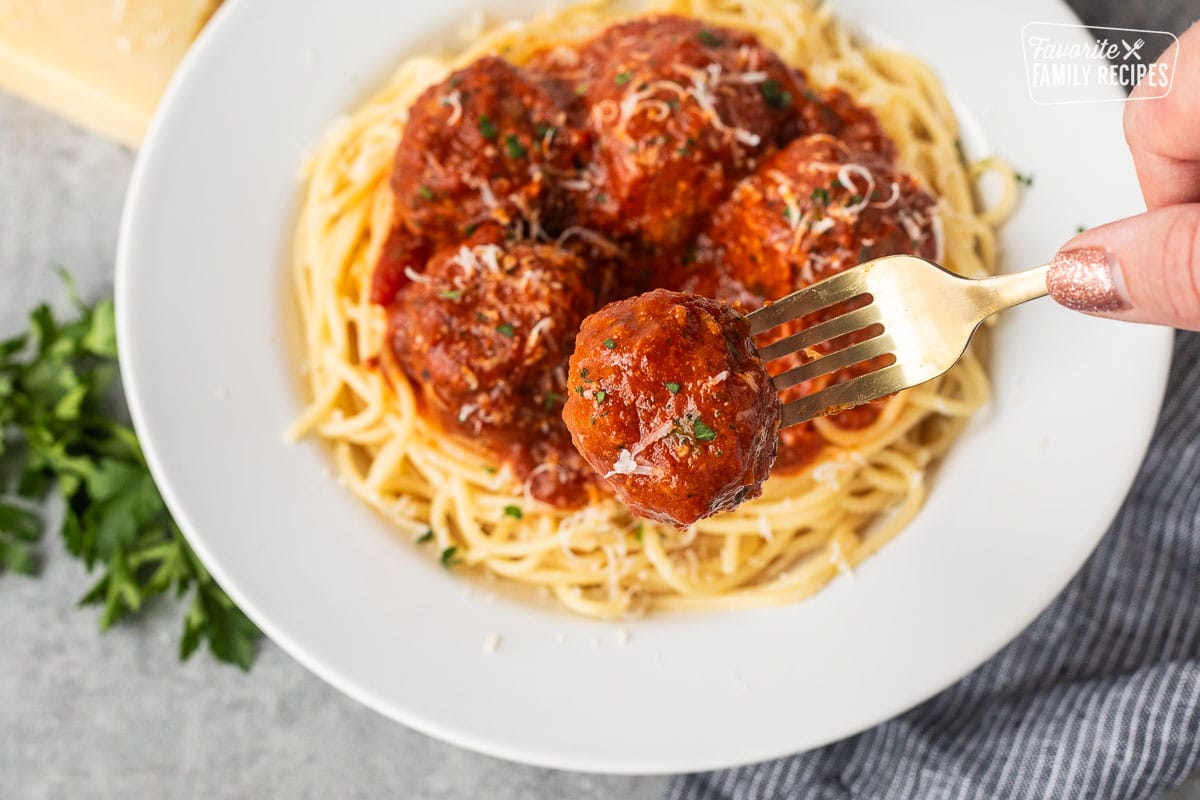 Fork holding onto an Instant pot meatball over a plate of spaghetti.