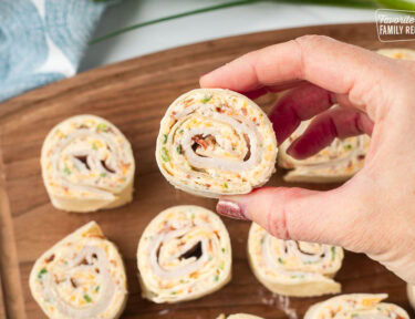 A hand holding a section of a pinwheel so show the creamy spiral center with bacon pieces and cheese