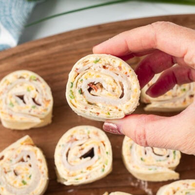 A hand holding a section of a pinwheel so show the creamy spiral center with bacon pieces and cheese