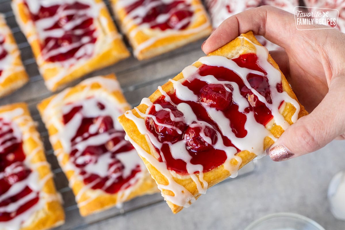 Hand holding a rectangle shaped cherry danish with white icing.