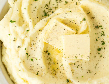 Bowl of mashed potatoes with fresh herbs, pepper, and butter.