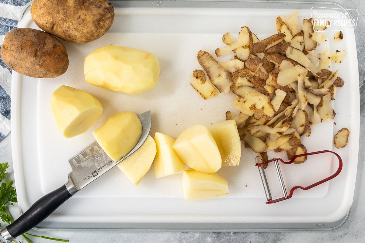 Cutting board with peeled and cut potatoes with a knife and peeler.